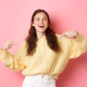 Girl in a yellow sweater pointing at herself. 