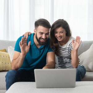 Couple looking at a computer screen, waving. 