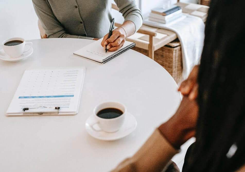 two people sat at table talking with one taking notes